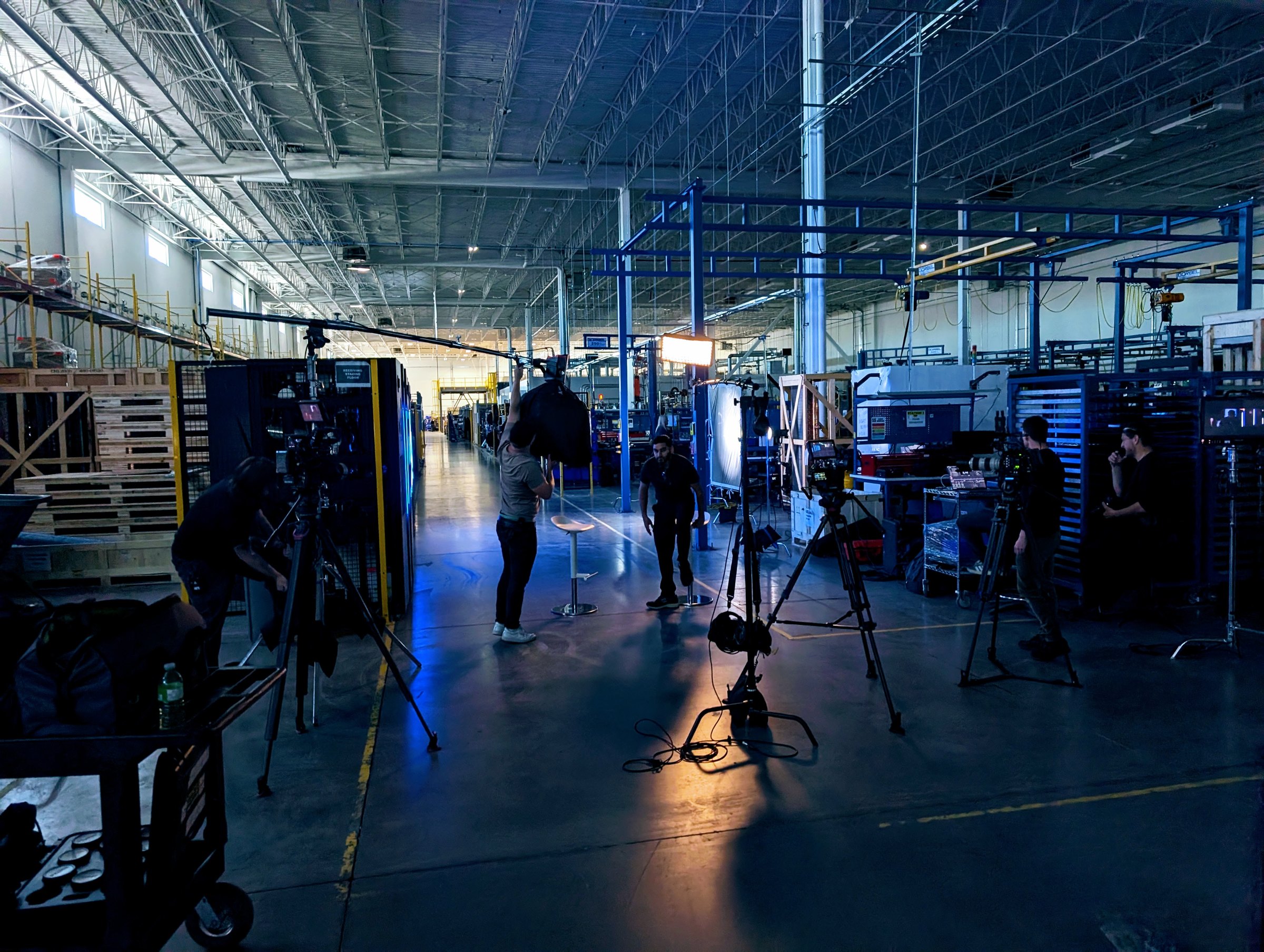 Wide behind-the-scenes of the crew setting up the fireside chat with both CEOs on the blue-lit set, CoolIT Calgary