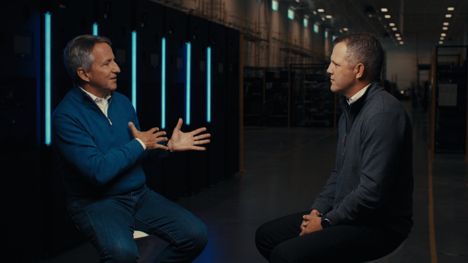 The finished two-shot of both CEOs in conversation on camera, cyan light bars behind them, CoolIT Calgary