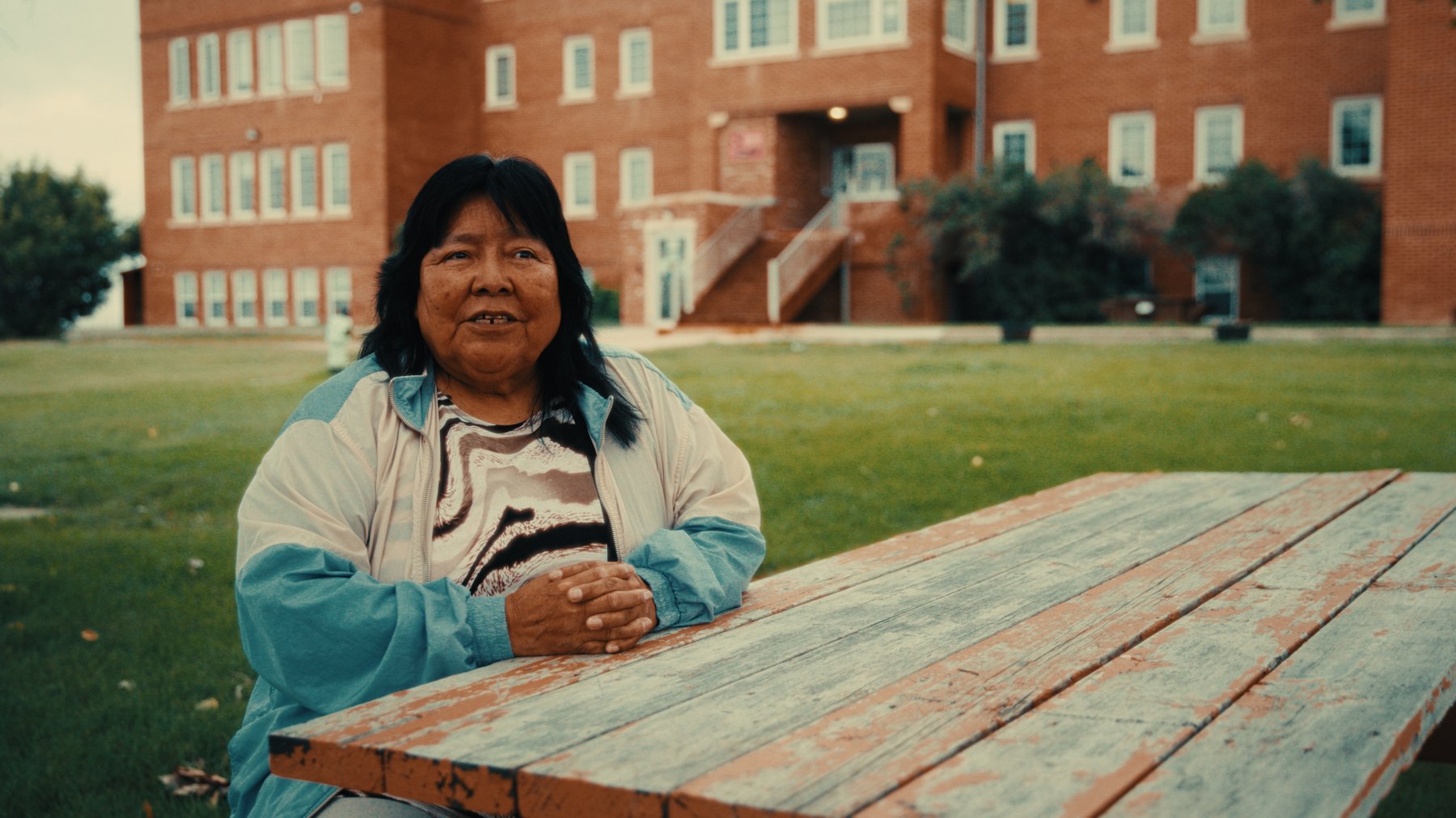 Founding-era staff member seated in front of Old Sun Community College — Natosapi documentary