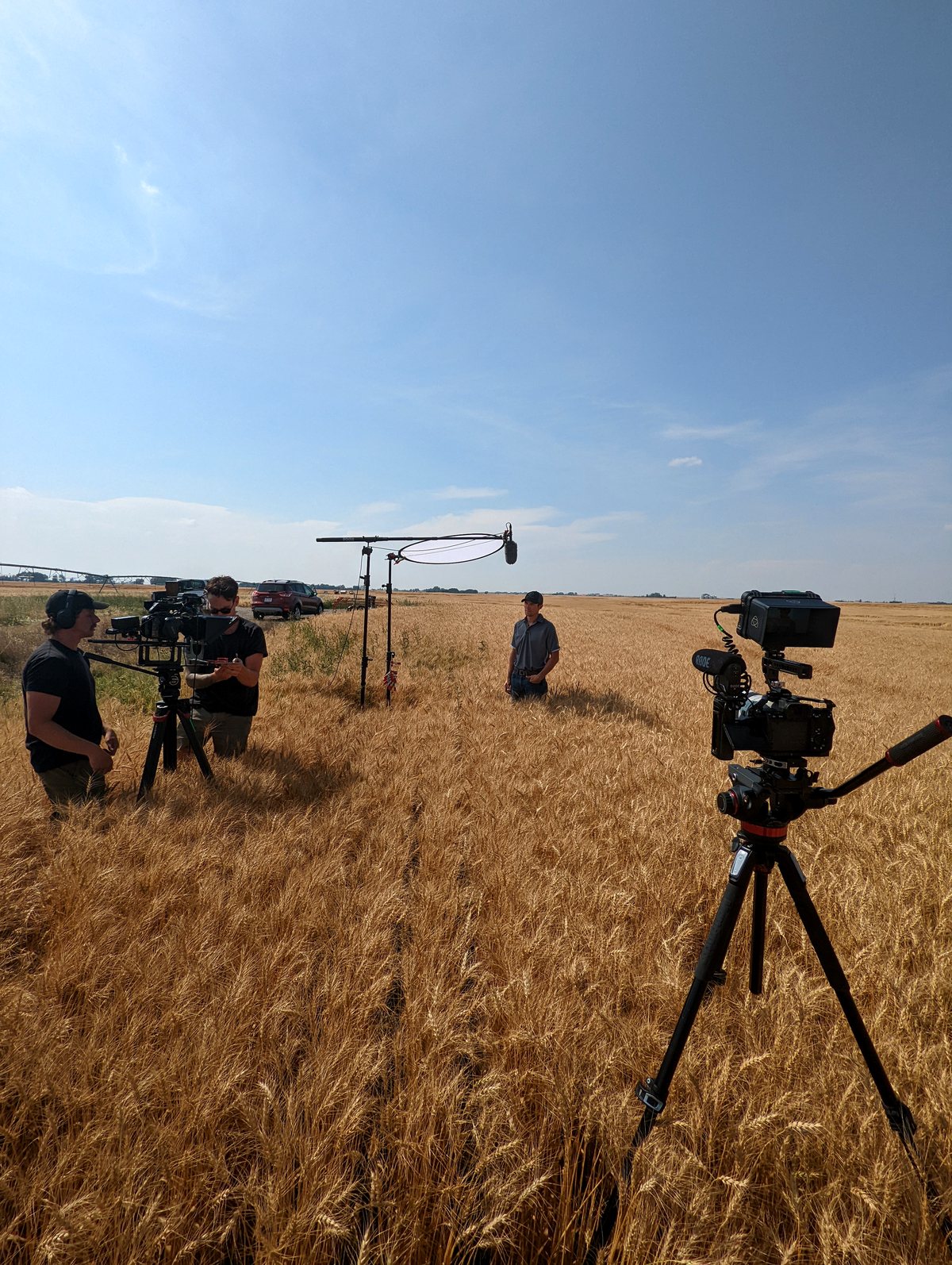 A small film crew shooting in a prairie field in Alberta, camera on a tripod under a big sky