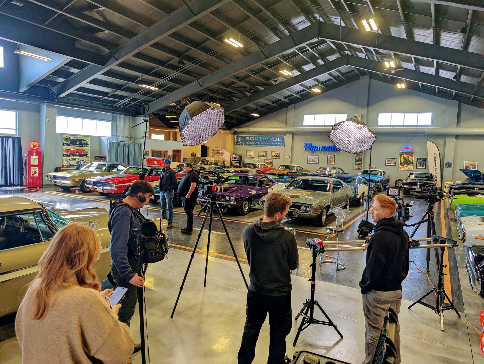 Film crew with lighting and grip gear shooting inside a classic car showroom, assembled by the DP