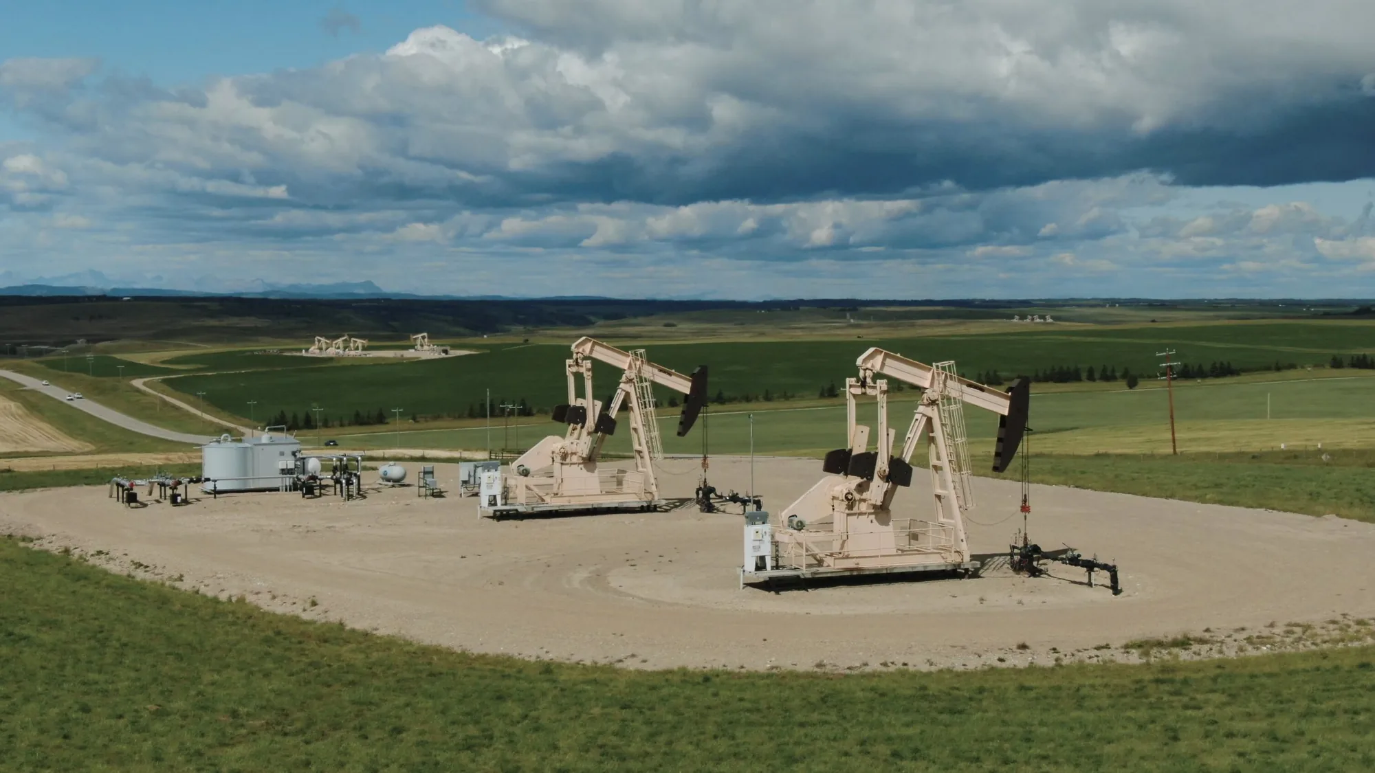 Pumpjacks on a wellsite pad with foothills behind, oil and gas drone photography Alberta