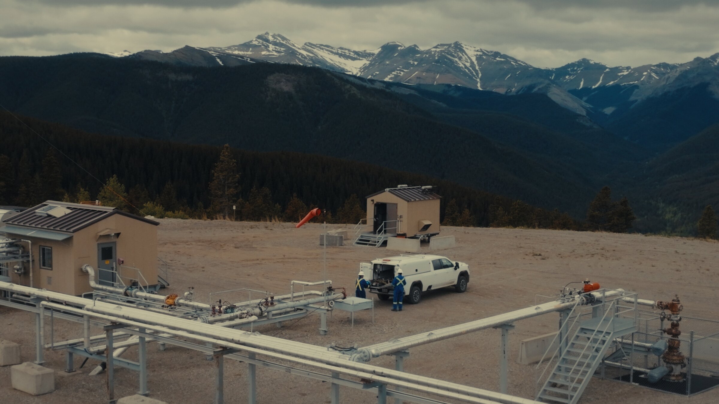 Aerial drone photo of an oil and gas wellsite with Rocky Mountain backdrop, Alberta