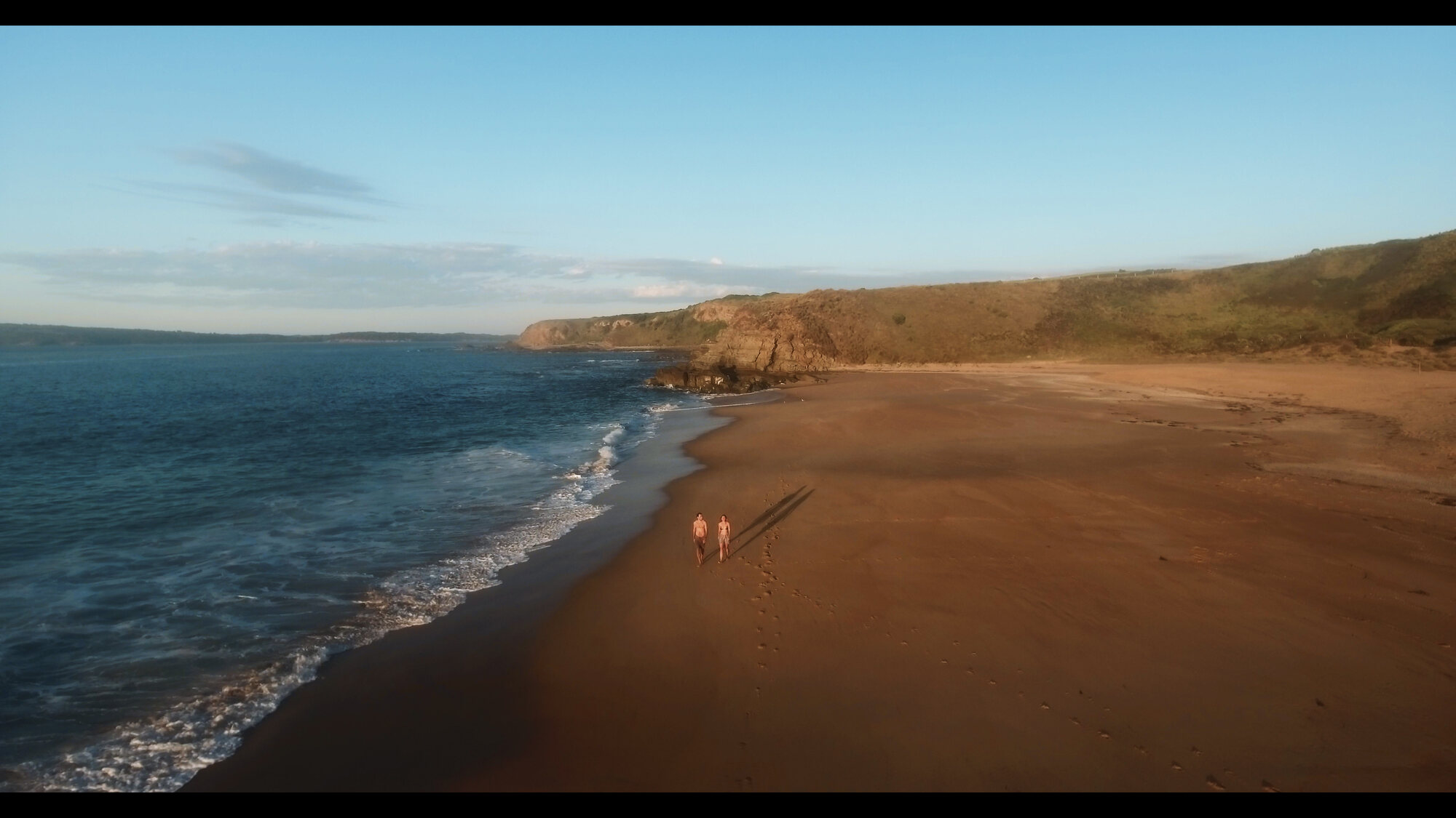 Couple walking a Phillip Island beach at golden hour, aerial tourism photo