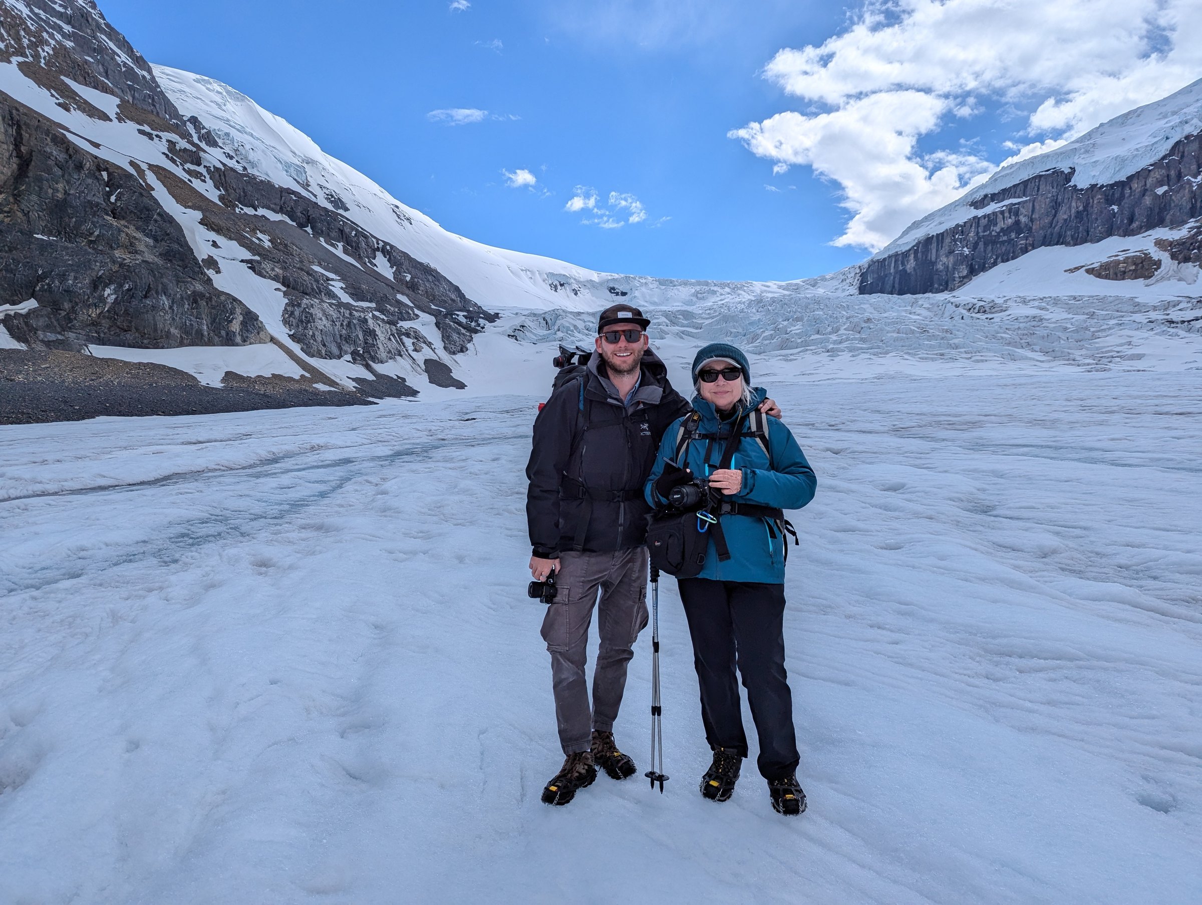 Dave Copithorne and Jan Kabatoff standing on Athabasca Glacier with ice field and mountains behind — June 2024