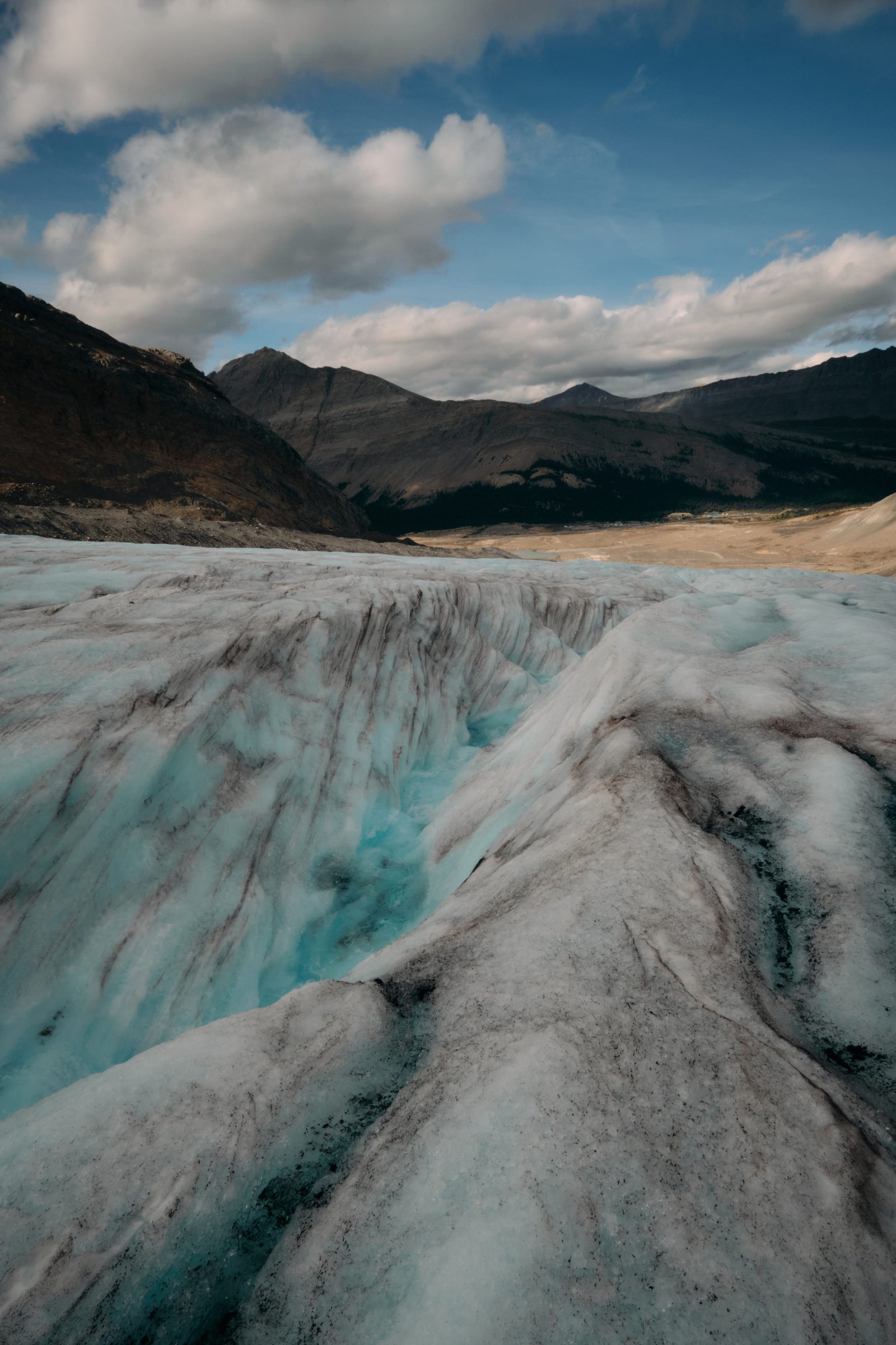 Deep blue crevasse system on Athabasca Glacier with mountain range beyond — August 2024