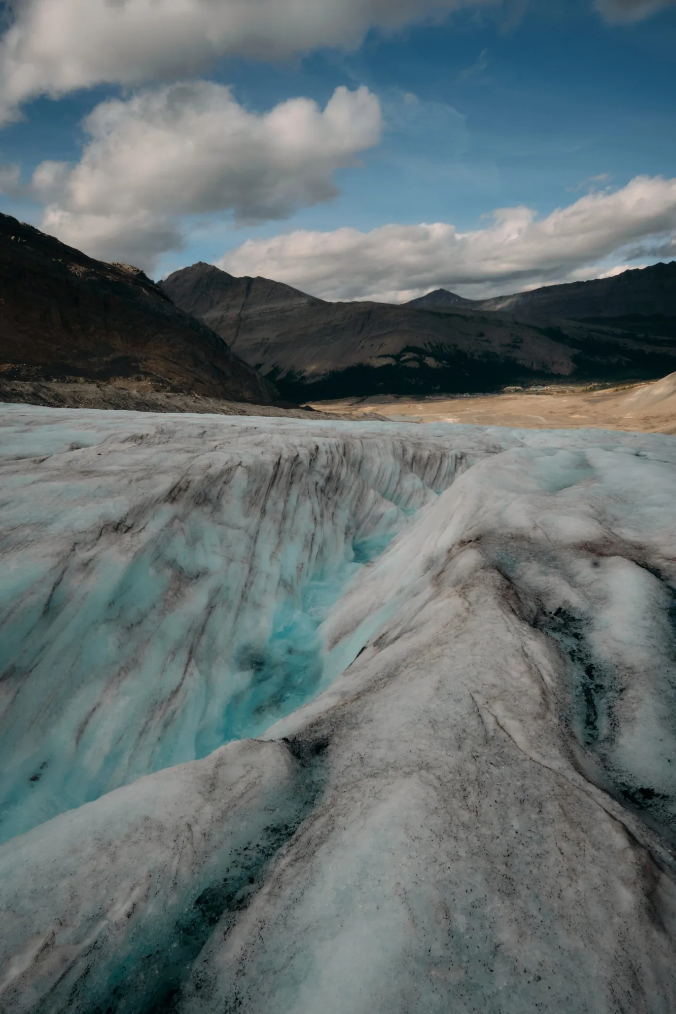 Deep blue crevasse system on Athabasca Glacier with mountain range beyond — August 2024
