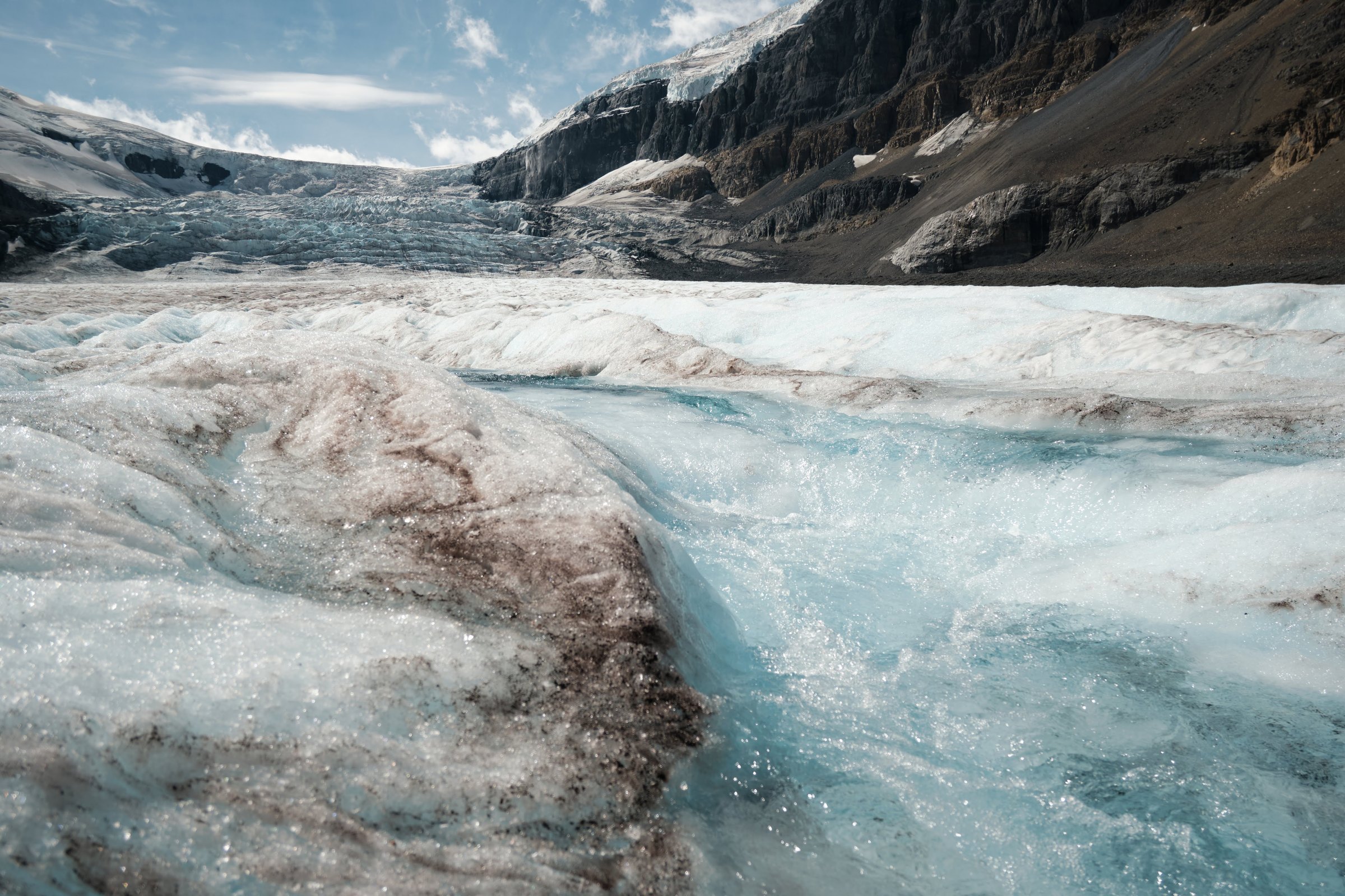 Glacial meltwater carving through Athabasca Glacier surface with mountain peaks beyond