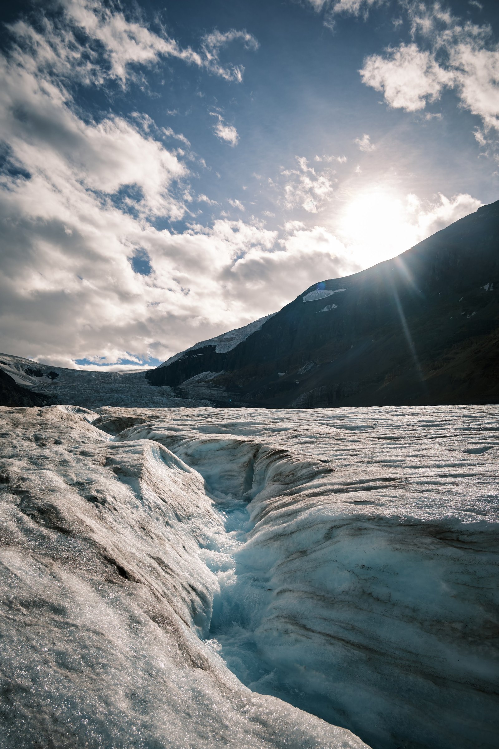 Meltwater channel on Athabasca Glacier with sun flare and mountain peaks — August 2024