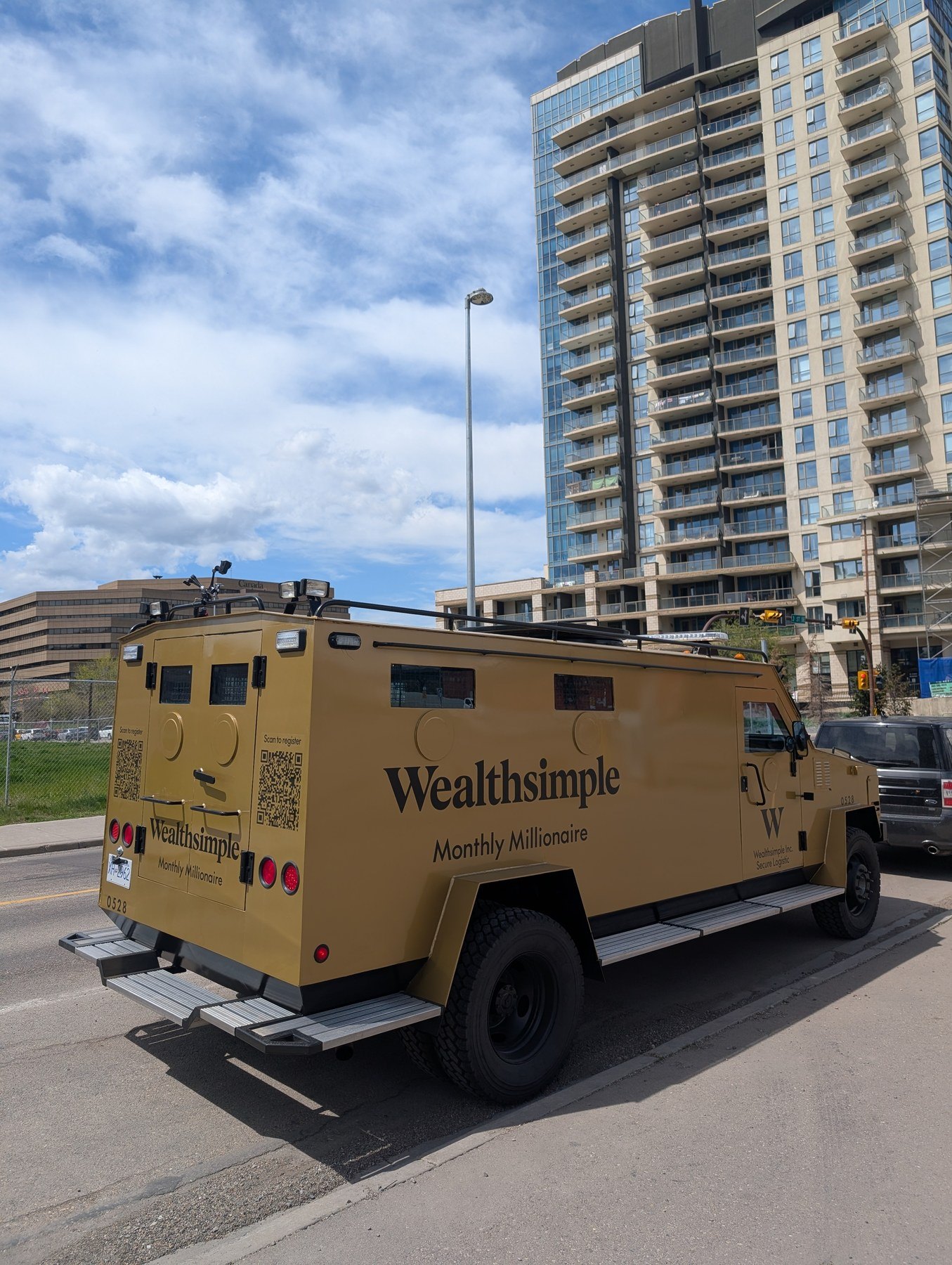 Wealthsimple Monthly Millionaire armored truck on Calgary street with downtown skyline behind — May 2026