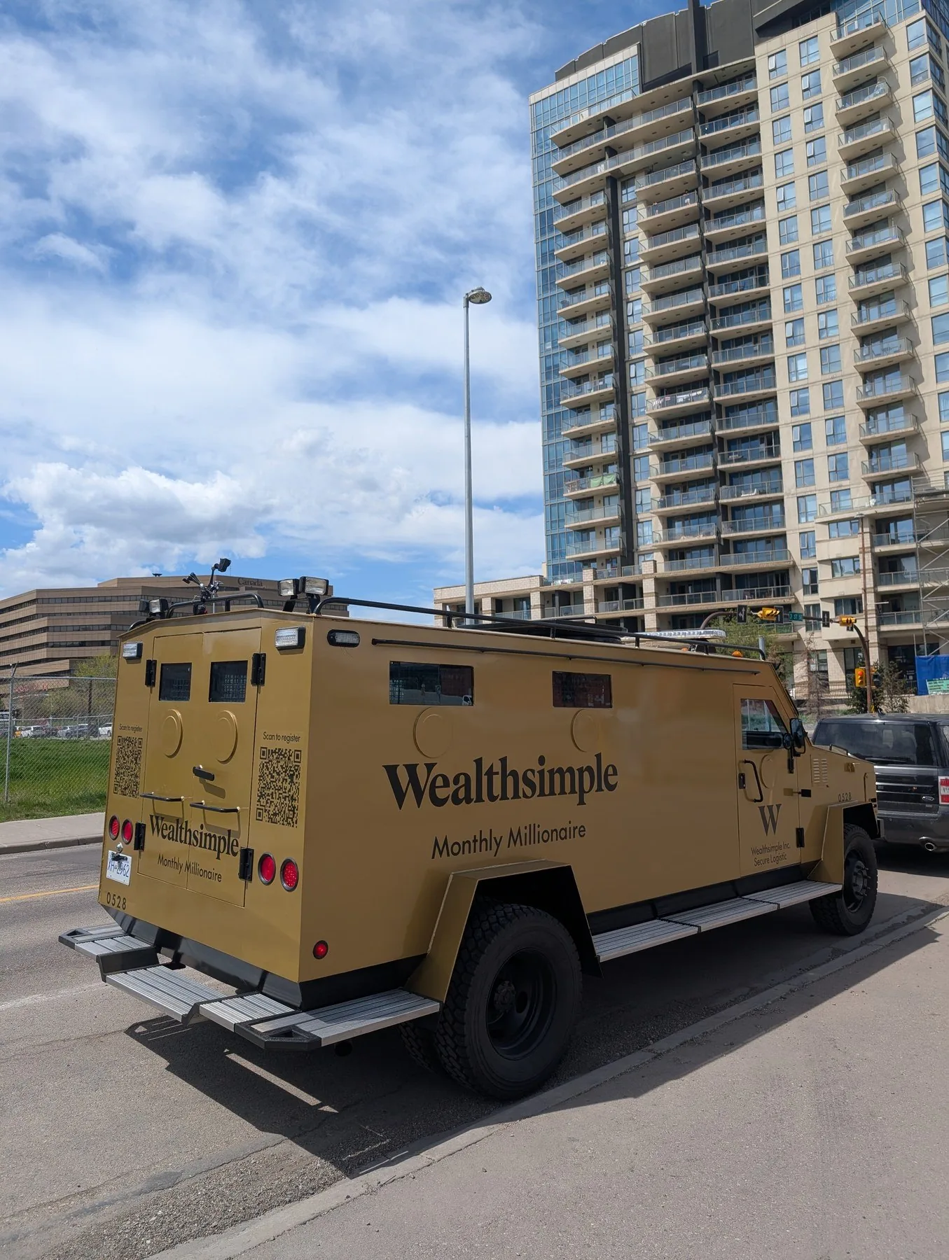 Wealthsimple Monthly Millionaire armored truck on Calgary street with downtown skyline behind — May 2026